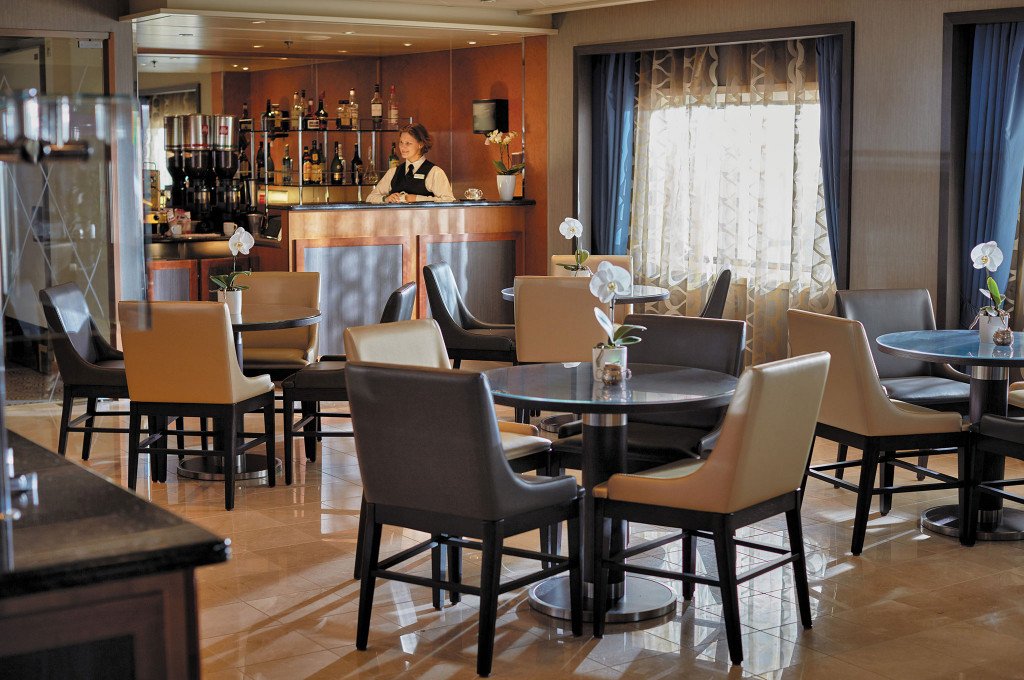 Coffee Connection mit Bar, Bistrotischen, Ledersesseln und Mitarbeiterin hinter der Theke.