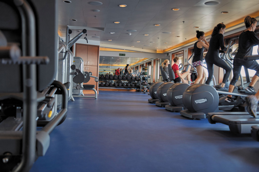 Fitness Center mit Crosstrainern, Kraftgeräten, Hantelablagen und mehreren Trainierenden.