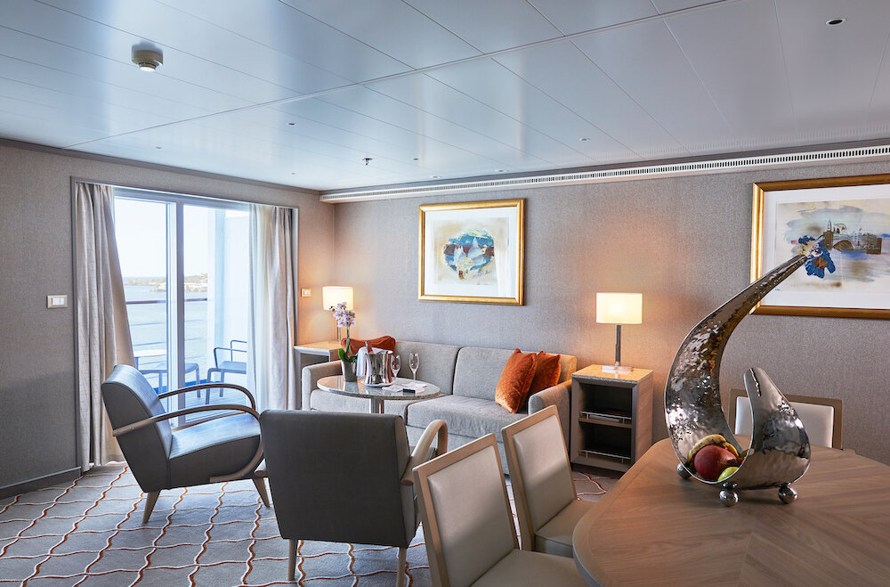Grand Suite Wohnbereich mit Sofa, Sesseln, Esstisch, goldgerahmten Kunstwerken und Balkon mit Meeresblick