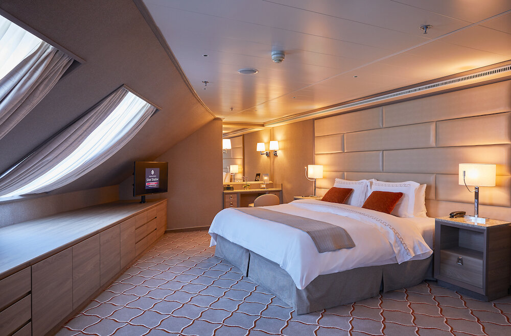 Grand Suite Schlafzimmer mit Doppelbett, Schminktisch, Schrägfenstern und warmer Beleuchtung an Bord