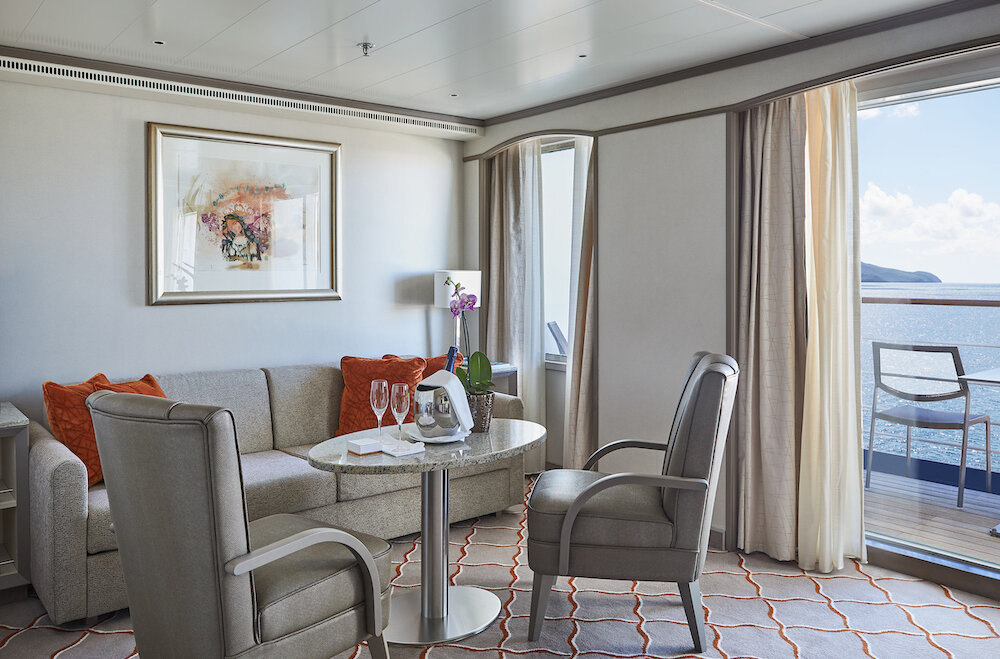 Wohnbereich einer Suite mit Sofa, Sessel und Balkon mit Meerblick sowie Champagner und Orchidee