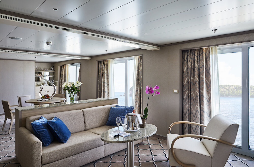 Wohnbereich der Owner's Suite mit Sofa, integrierter Bar und Balkon mit Küstenblick