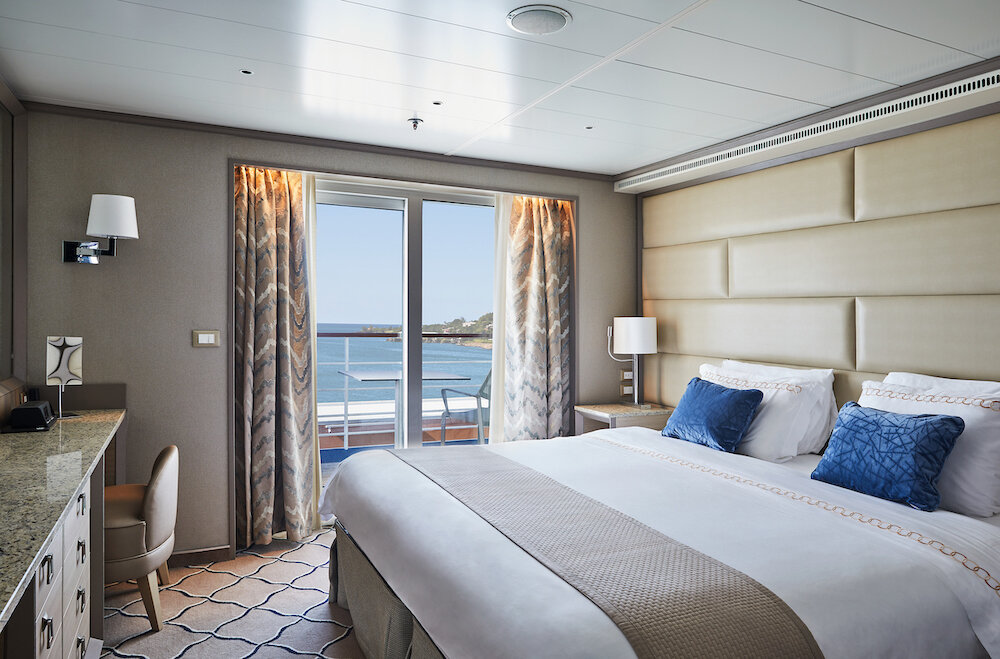 Schlafzimmer der Owner's Suite mit Doppelbett, blauen Kissen und Balkon mit Meerblick
