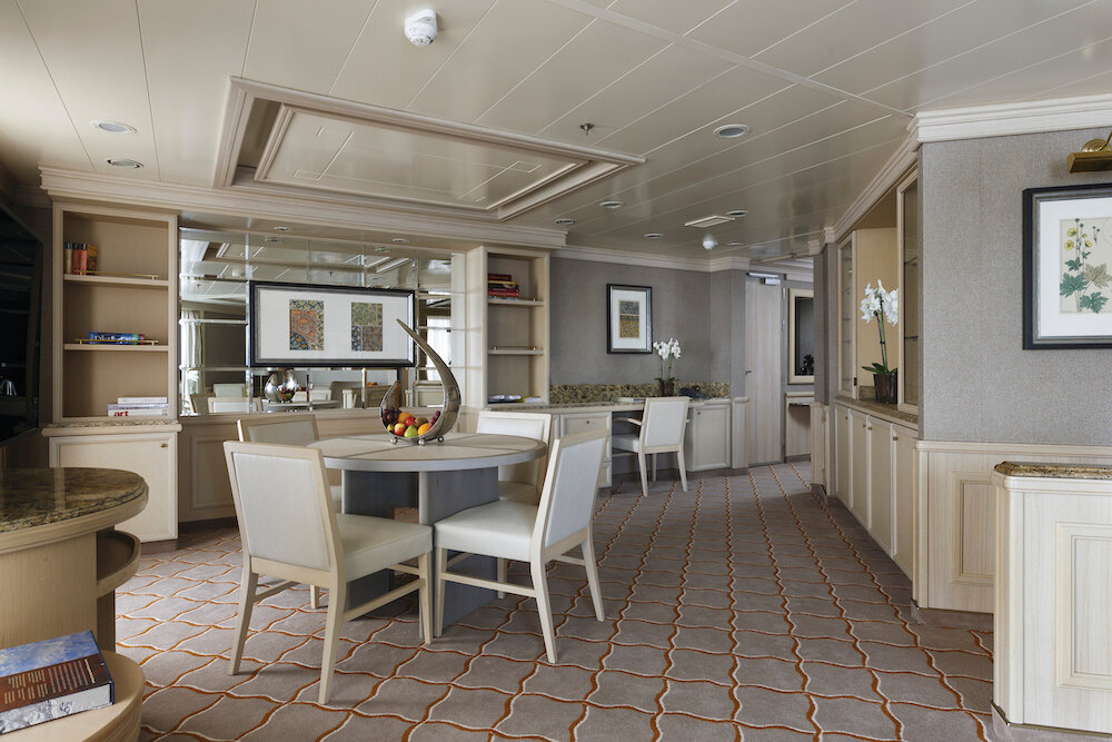 Wohnzimmer einer Grand Suite mit Esstisch, Regalwand und klassischer Einrichtung auf einem Luxuskreuzfahrtschiff