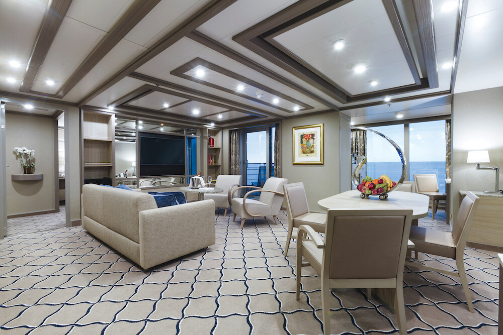 Großzügiger Wohn- und Essbereich einer Owner's Suite mit Sofa, Esstisch und Panoramafenstern mit Meerblick