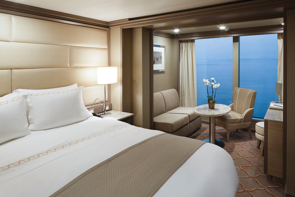Elegantes Suiten-Schlafzimmer mit Doppelbett, gepolstertem Kopfteil und Balkon mit Meeresblick auf einem Luxuskreuzfahrtschiff
