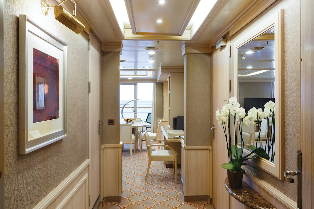 Eleganter Eingangsflur einer Royal Suite mit Orchideen, Kunstwerk und Blick auf den Essbereich mit Meerblick