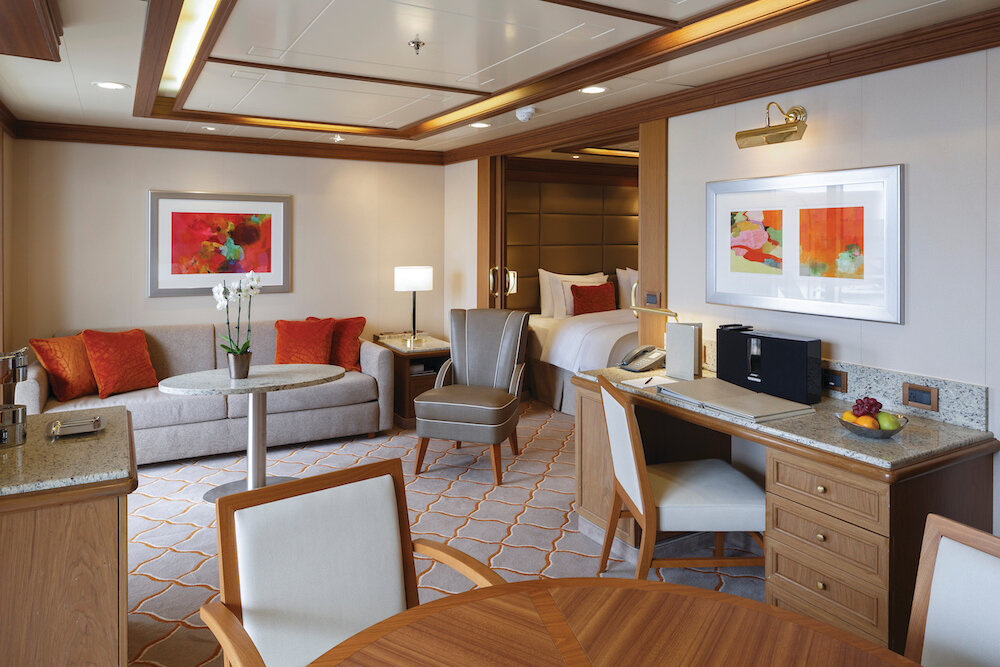 Weitläufige Suite mit Sofa, Schreibtisch, Holzvertäfelung und farbenfrohen Kunstwerken an den Wänden an Bord