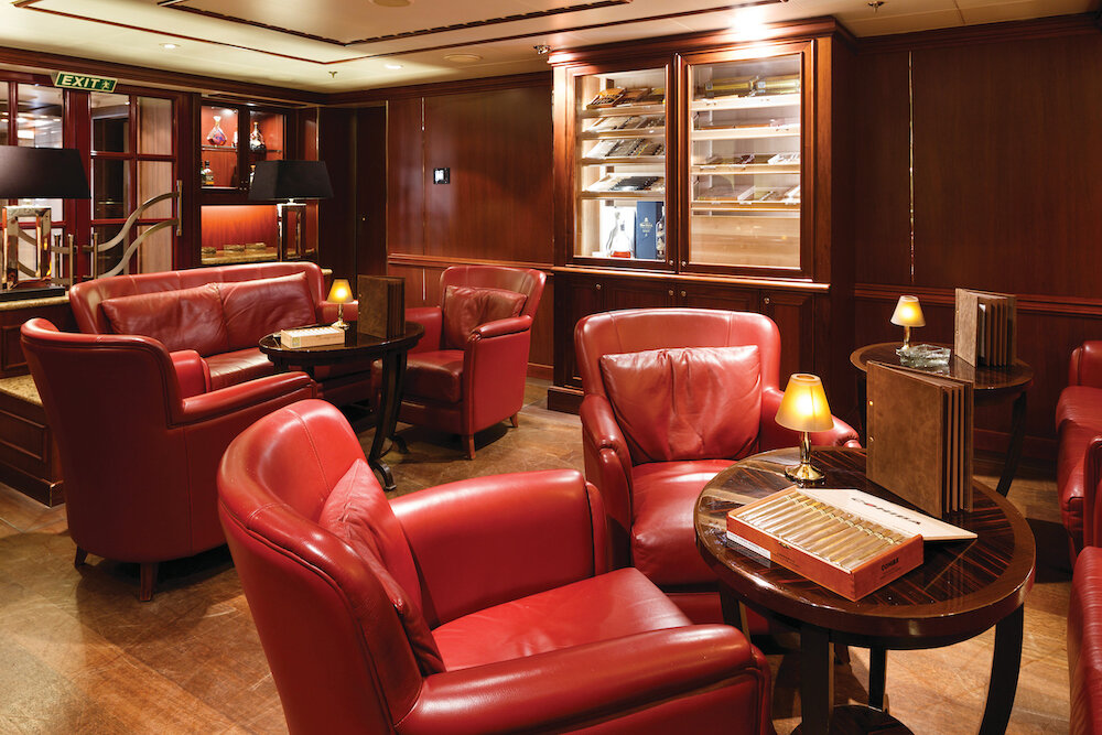 Connoisseur's Corner auf der Silver Spirit mit roten Ledersesseln, beleuchteten Humidoren und klassischem Holzinterieur.
