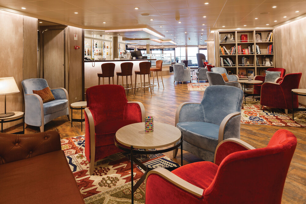 Elegante Arts Café Lounge mit Sesseln, Regalen und Holzausstattung auf einem Schiff.