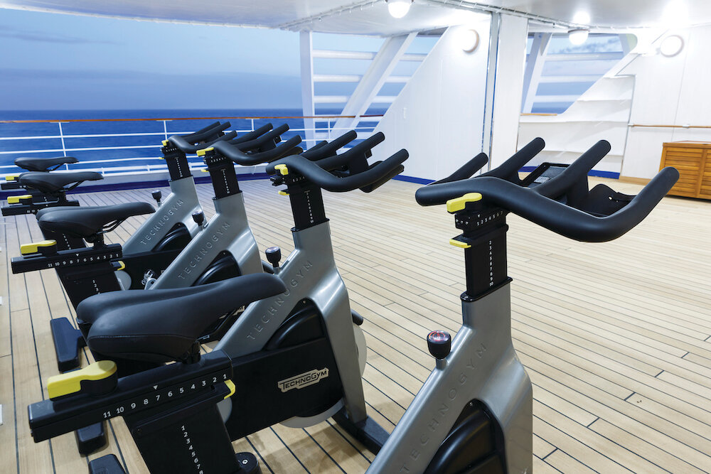 Spinning-Bikes von Technogym auf einem halboffenen Außendeck der Silver Spirit mit Meeresblick in der Abenddämmerung