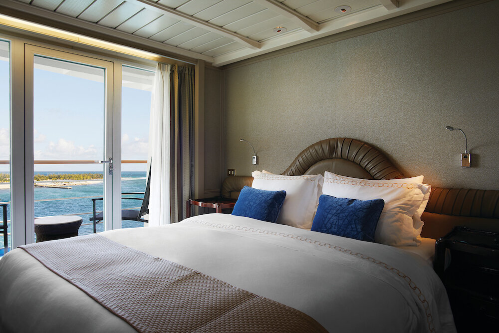 Schlafbereich einer Grand Suite mit Doppelbett, Schminktisch und Balkon mit Meerblick auf einem Expeditionskreuzfahrtschiff