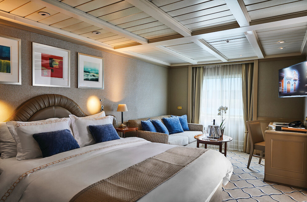 Luxuriöser Suite-Schlafbereich mit Doppelbett, gewölbtem Lederkopfteil, Sofa, Orchidee und kassettierter Holzdecke