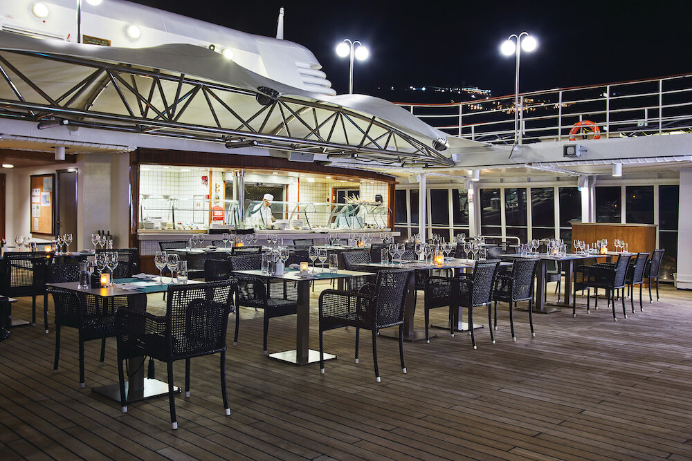 Außenrestaurant mit offener Küche auf dem Deck eines Expeditionsschiffes bei Nacht mit Kerzen auf den Tischen