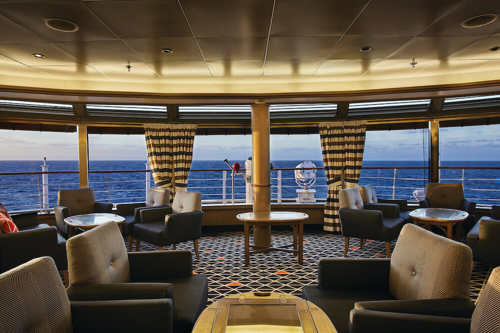 Observation Lounge mit Sesseln, runden Tischen und Panoramafenstern mit Meerblick auf einem Expeditionskreuzfahrtschiff