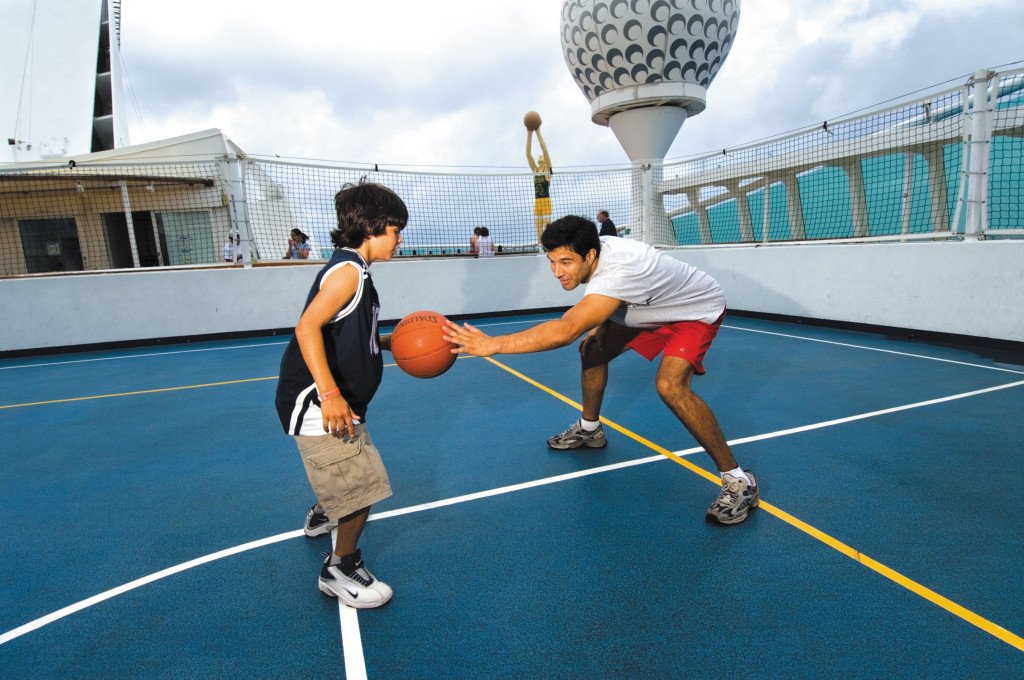 Junge und Mann spielen Basketball auf dem Außensportplatz an Bord der Voyager of the Seas.