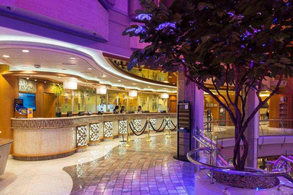 Guest Service Rezeptionsschalter mit Beleuchtung und Atrium-Design auf der Voyager of the Seas.