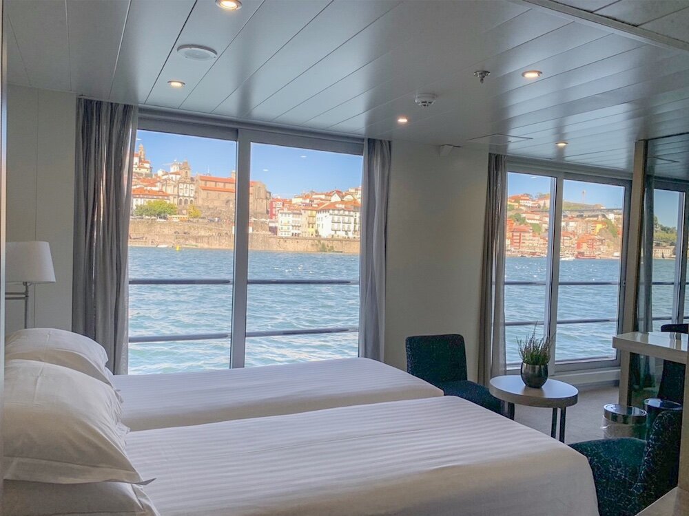 Suite mit Doppelbett, Sitzgruppe und Panoramafenstern mit Blick auf den Douro und die Altstadt von Porto.