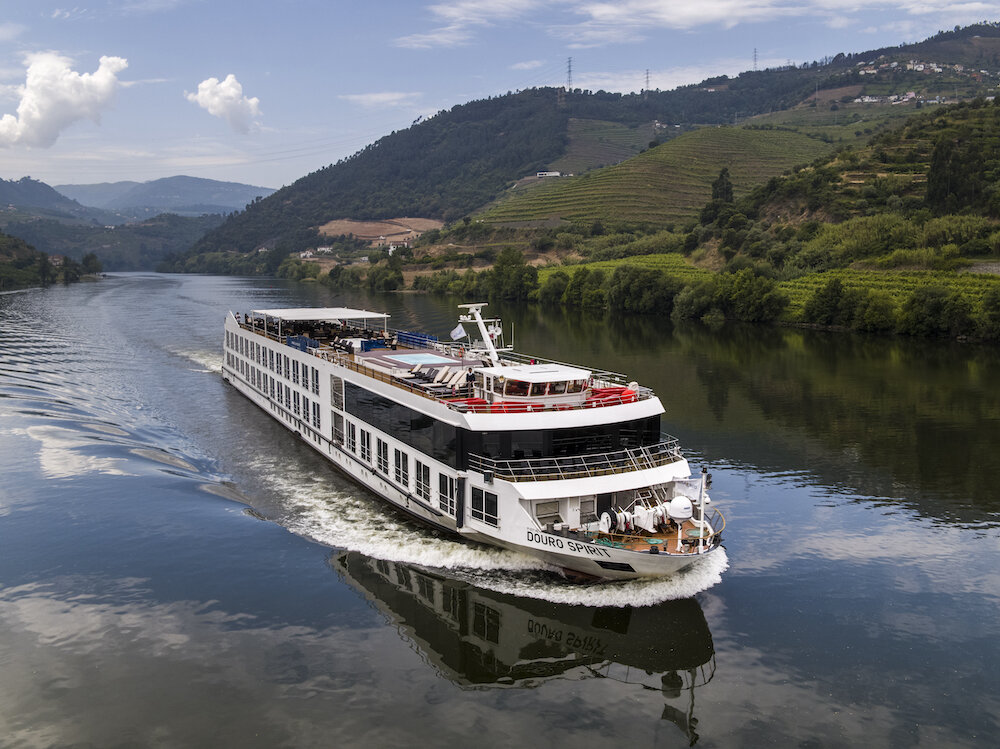 Flusskreuzfahrtschiff in Fahrt auf dem Douro zwischen terrassierten Weinbergen.