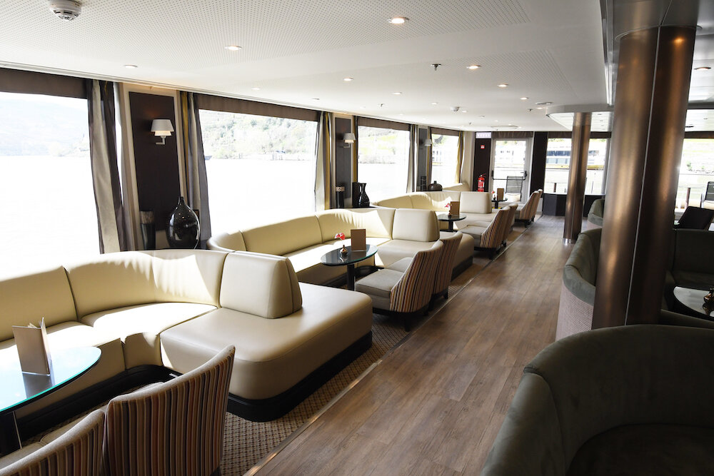 Panorama-Salon mit Sitzlandschaften, Sesseln und großen Fenstern mit Blick auf den Fluss.