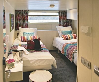Zweibettkabine auf dem Hauptdeck eines Flusskreuzfahrtschiffes mit bunten Kissen, Sektkühler und Fenster