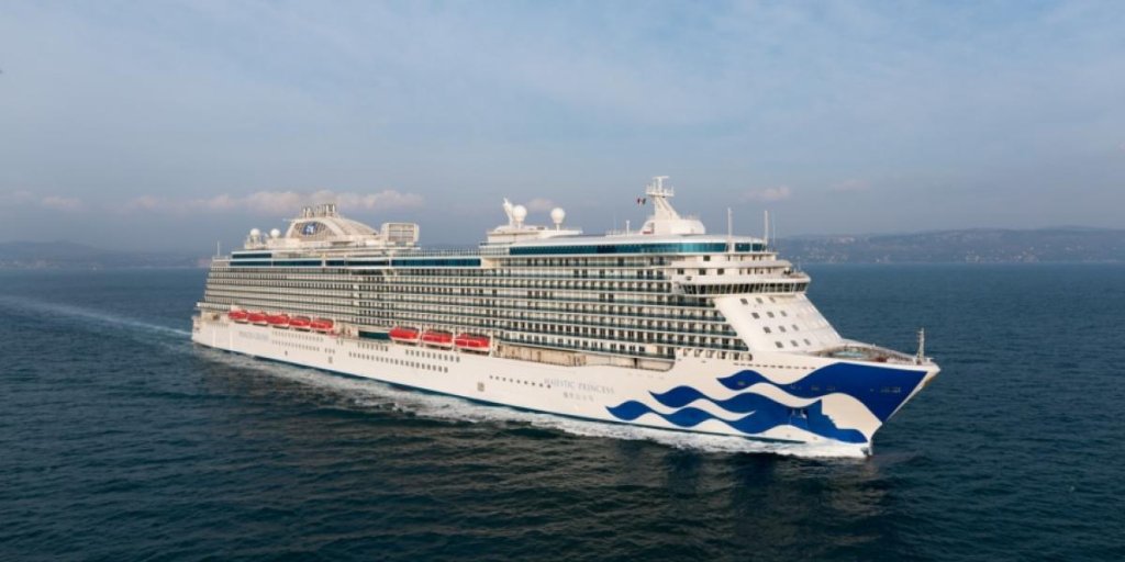 Großes Kreuzfahrtschiff mit weißem Rumpf und blauen Wellenlinien bei der Fahrt auf offener See