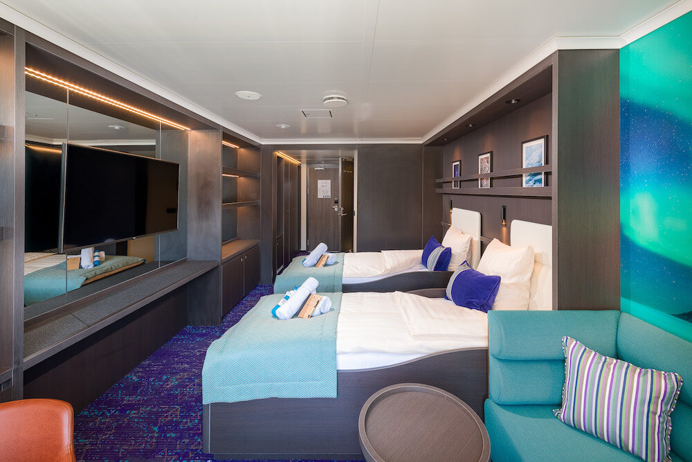 Deluxe-Doppelkabine mit zwei Einzelbetten, Sofa, Schreibtischzeile und Fernseher an der Spiegelwand.