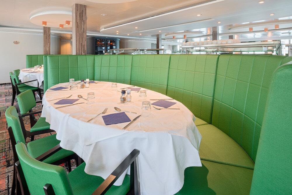 Speisesaal eines Expeditionsschiffs mit eingedecktem Tisch, halbrunder Sitzbank und Buffetstation im Hintergrund.