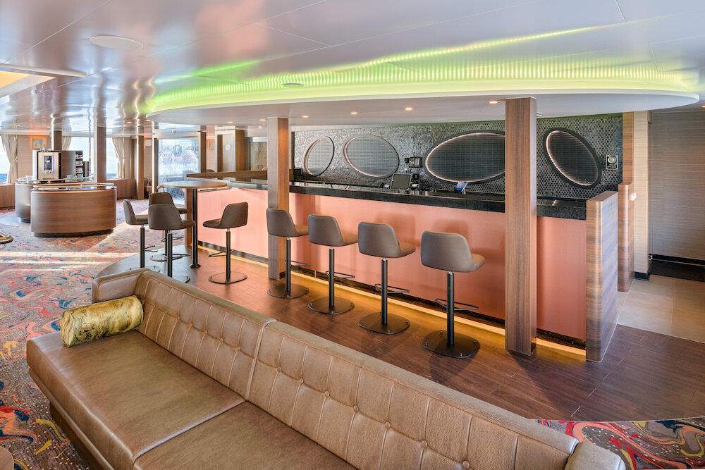 Bar in der Aussichtslounge eines Expeditionsschiffs mit Bartresen, Barhockern, Stehtischen und langem Ledersofa.