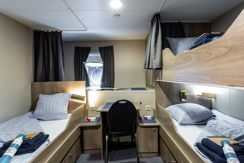 Dreibettkabine mit Etagenbett, Einzelbett, Schreibtisch und Bullauge an Bord eines Expeditionsschiffes