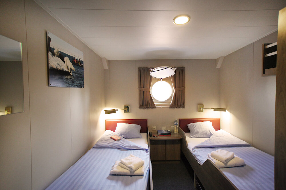 Doppelkabine mit zwei Einzelbetten, Nachttisch und Bullauge an Bord eines Expeditionsschiffes