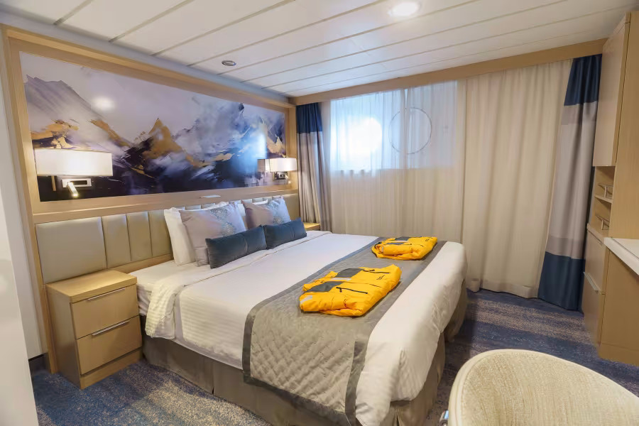 Einzelkabine mit Doppelbett, dekorativem Berggemälde und orangefarbener Expeditionsjacke auf dem Bett