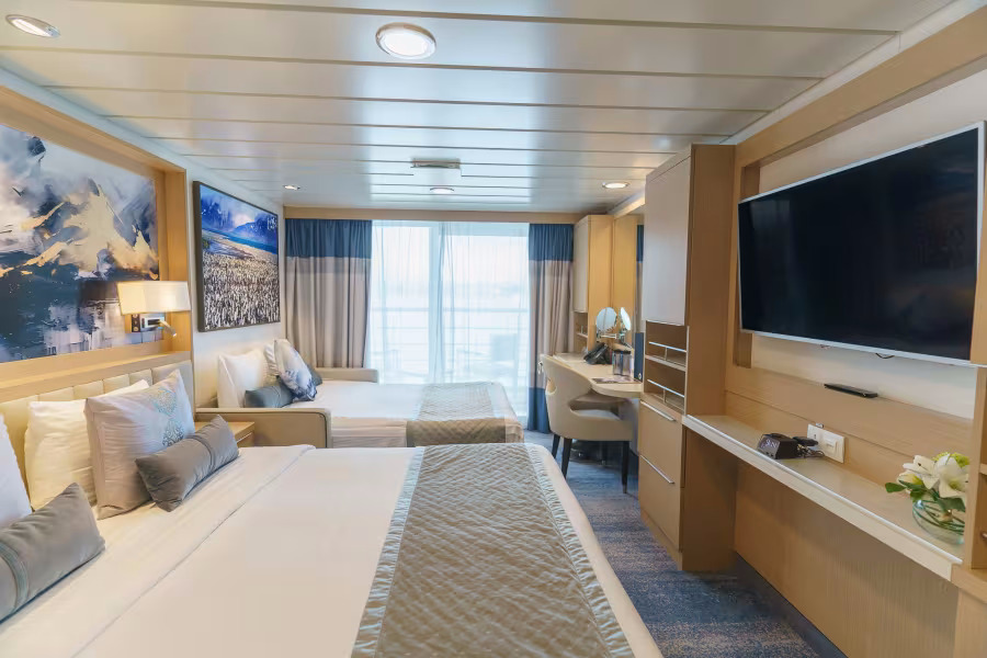 Geräumige Suite mit Doppelbett, Einzelbett, Schreibtisch und Pinguingemälde auf einem Expeditionskreuzfahrtschiff
