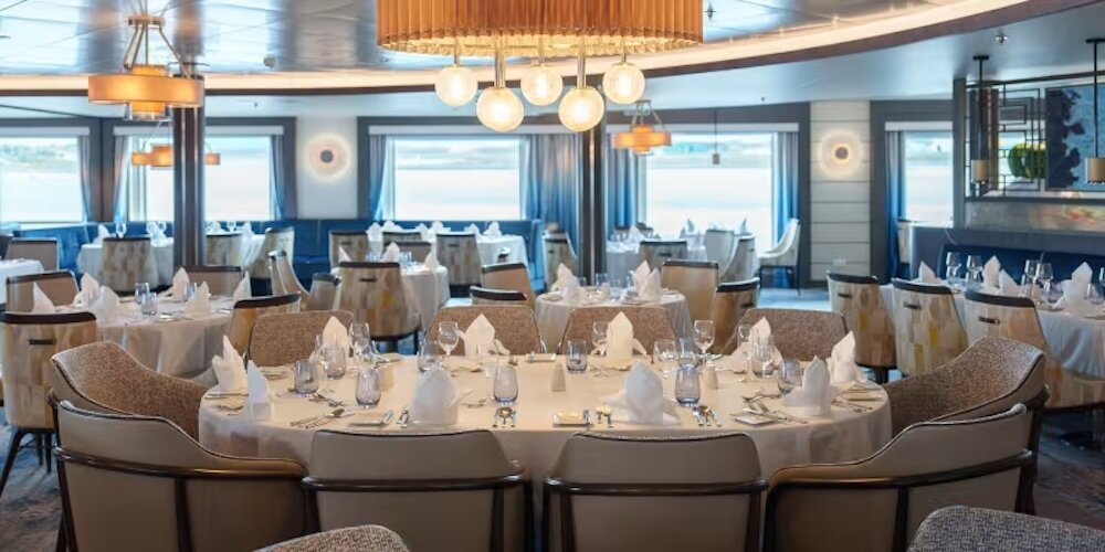 Elegantes Hauptrestaurant mit gedeckten Rundtischen, Kronleuchter und Panoramafenstern mit Wasserblick