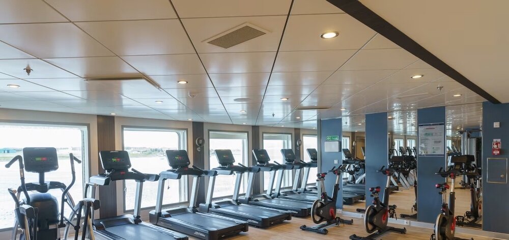 Fitnesscenter mit Laufbändern und Fahrrädern mit Blick auf das Wasser durch große Panoramafenster