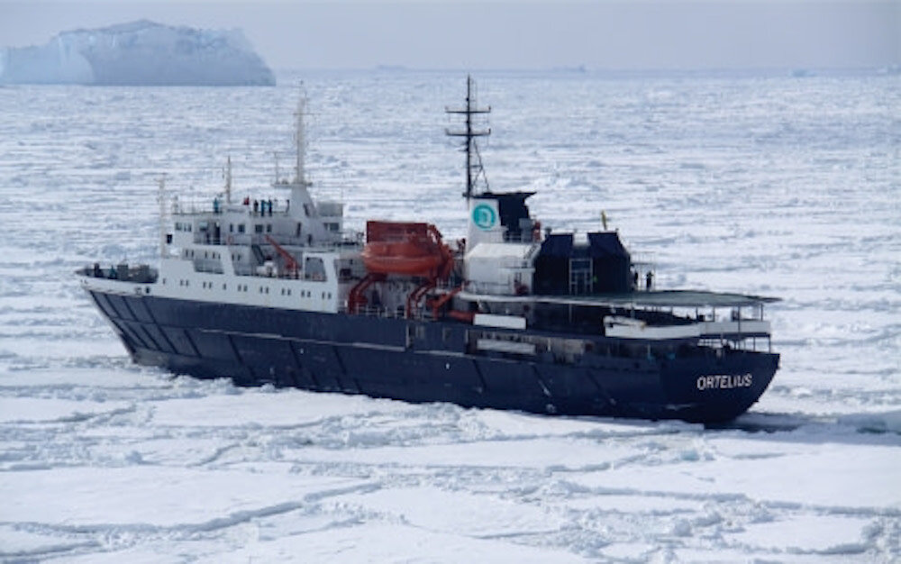 Expeditionsschiff Ortelius fährt durch dichtes Packeis, im Hintergrund ein Tafeleisberg.