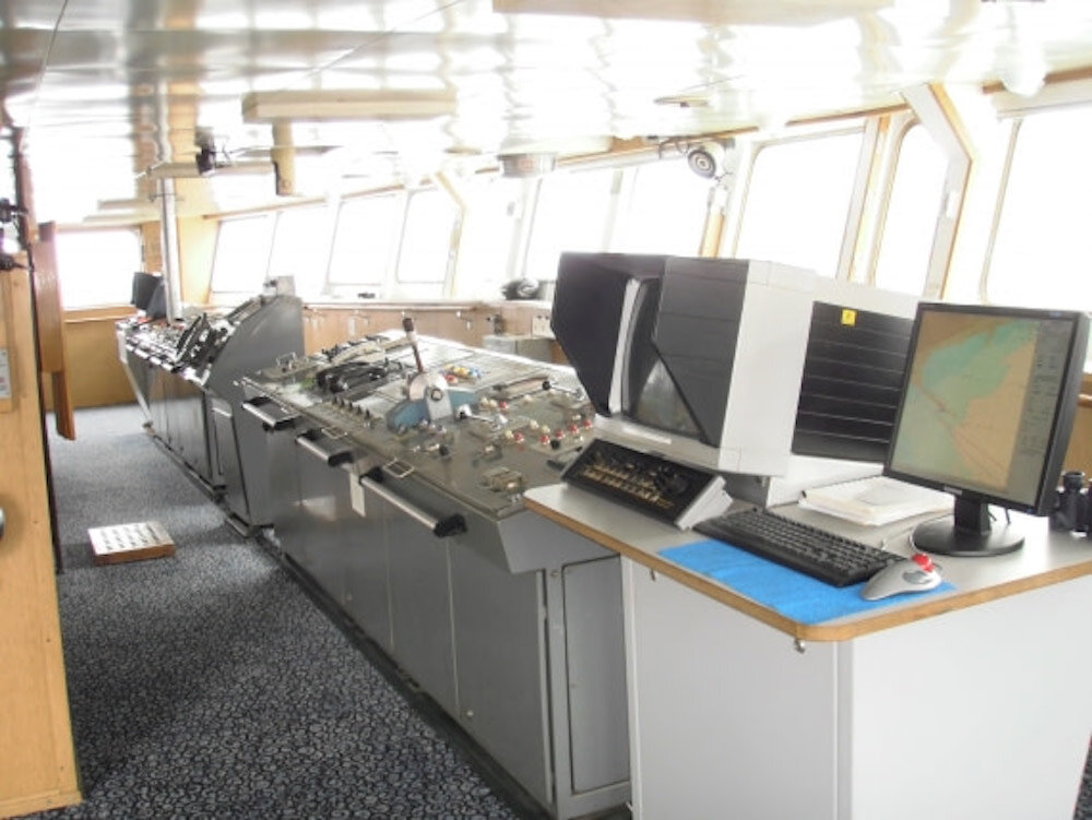 Kommandobrücke eines Expeditionsschiffs mit Steuerpult, Navigationsmonitoren und umlaufenden Fenstern.