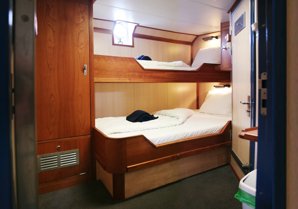 Doppelkabine mit Etagenbett aus Holz, Bullauge und Kleiderschrank an Bord eines Expeditionssegelschiffes