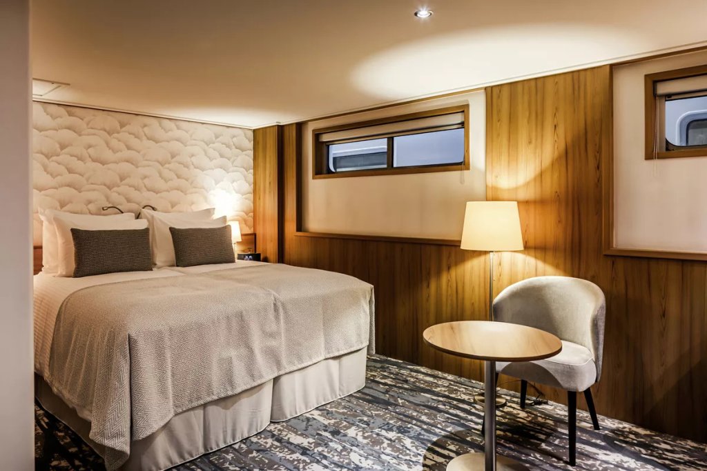 Doppelkabine auf dem Hauptdeck mit Doppelbett, gestepptem Kopfteil, Sitzecke und schmalen Fenstern über Holzvertäfelung