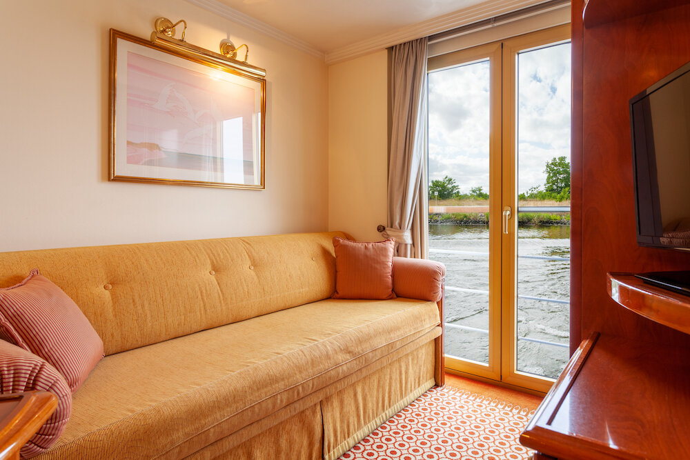 Einzelkabine auf dem Oberdeck mit Sofabett, Wandbild und französischem Balkon mit Blick auf den Fluss