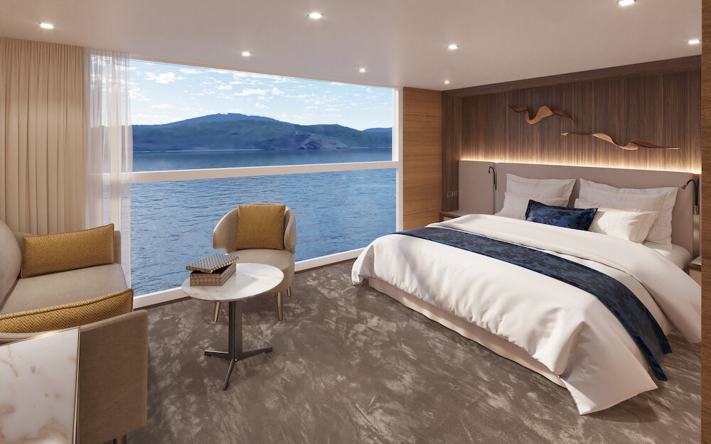 Luxuriöse VIP-Kabine auf der Thurgau Gold mit großem Doppelbett, Panoramafenster und Blick auf eine bergige Flusslandschaft, modern eingerichtet mit Holzakzent-Wand, indirekter Beleuchtung, Lesesessel und Marmortisch.