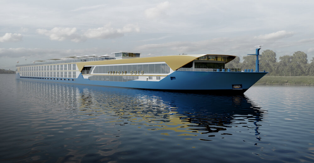 Außenansicht des modernen Flusskreuzfahrtschiffs Thurgau Gold von Thurgau Travel mit blauem Rumpf und goldfarbenem Aufbau, das ruhig auf einem Fluss unter leicht bewölktem Himmel liegt.
