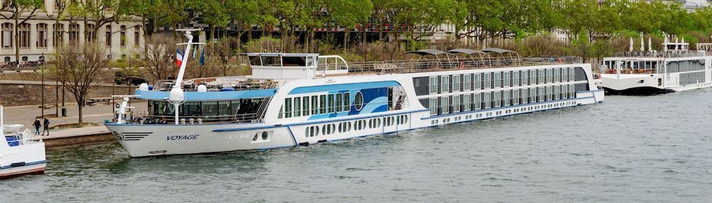 Flusskreuzfahrtschiff Voyage an einer von Bäumen bestandenen Uferpromenade in Frankreich, dahinter ein weiteres Flussschiff.