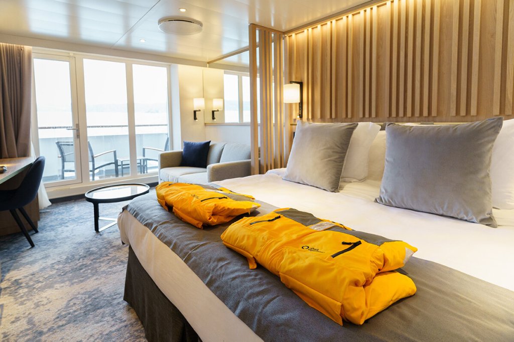 Balcony Suite der Ultramarine mit Doppelbett, orangefarbenen Expeditionsparkas und Balkon mit Naturblick.