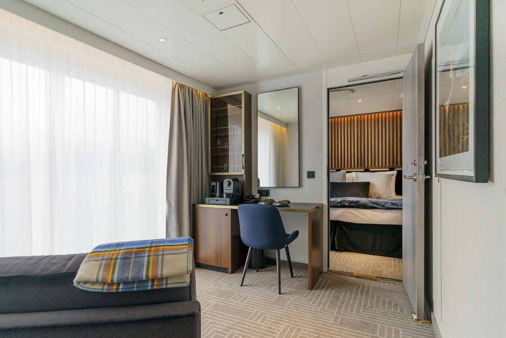 Owner's Suite der Ultramarine mit Wohnbereich, Sofa, Schreibtisch und breitem Panoramafenster mit Naturblick.