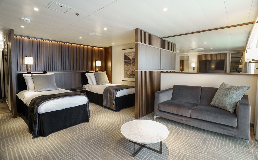Penthouse Suite der Ultramarine mit zwei Einzelbetten, Sofa, Holzlamellentrennwand und modernem Wohnbereich.