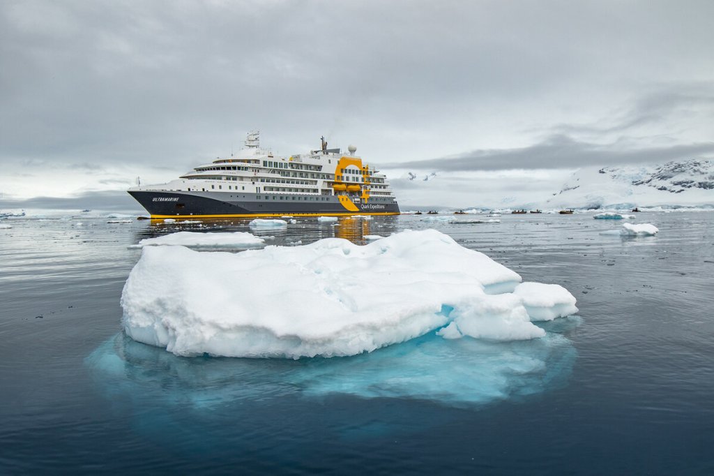 Expeditionsschiff in antarktischen Gewässern mit Eisberg im Vordergrund und Zodiac-Booten auf dem Wasser