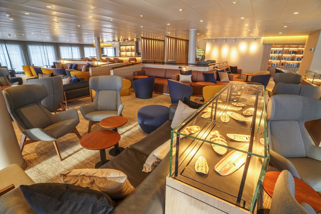Panorama Lounge & Bar der Ultramarine mit zahlreichen Sesseln, Sofas, Bar und beleuchteter Vitrine mit Expeditionsausrüstung.