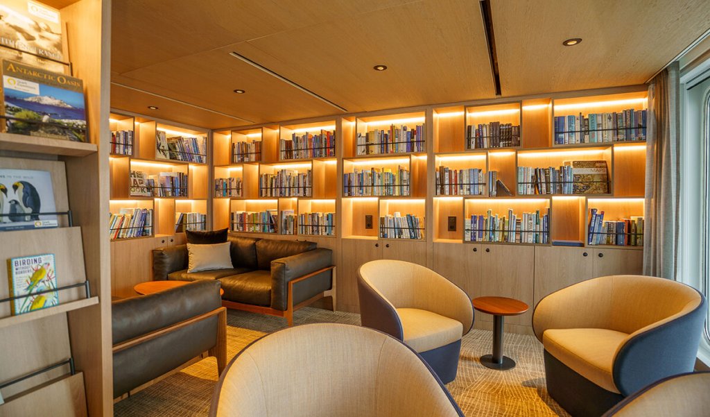 Gemütliche Bibliothek der Ultramarine mit beleuchteten Bücherregalen voller Naturführer und Polarexpeditionsliteratur.