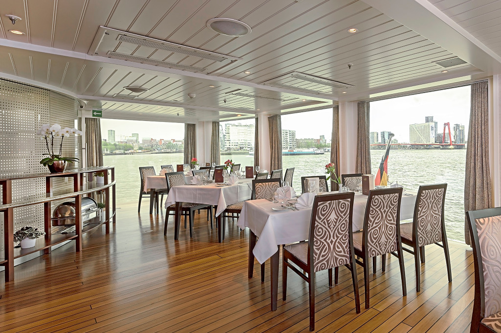 Helles Bordrestaurant mit eingedeckten Tischen, gemusterten Stühlen und Panoramafenstern mit Blick auf die Stadt am Fluss